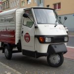 Kleintransporter Mit Drei Rädern Parkt Auf Einer Stadtstraße Neben Gehweg Und Weiteren Autos.
