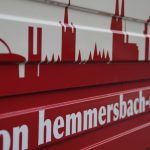Rotes Und Weißes Schild Mit Stadtsilhouette Und Dem Schriftzug Von Hemmersbach-Druck.de Am Unteren Rand.