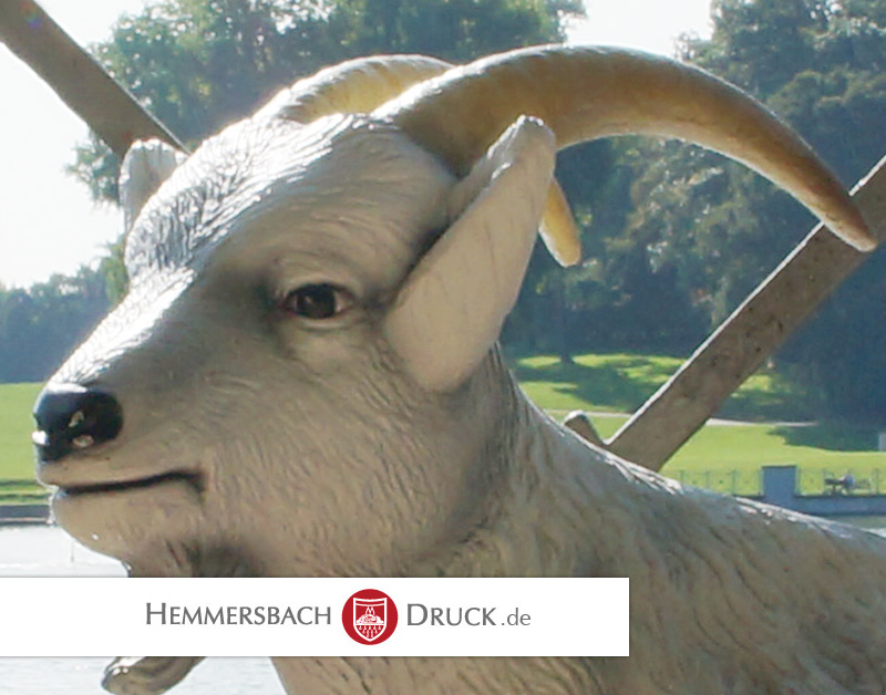 Weiße Ziegenstatue Mit Gebogenen Hörnern Steht Im Park, Bäume Im Hintergrund, Unten Logo Und Text.