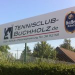 Schild Des Tennisclubs Buchholz Mit Getränke-Logos An Zaun, Im Hintergrund Bäume Und Wohnhäuser.