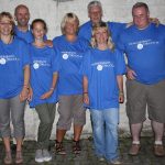 Sechs Erwachsene Und Ein Kind Stehen In Blauen Hammersbach Druck T-Shirts Zusammen Vor Einer Wand.