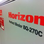 Bindemaschine Horizon Perfect Binder Bq-270C Steht In Nahaufnahme Mit Roter Und Schwarzer Beschriftung Auf Grauer Oberfläche.