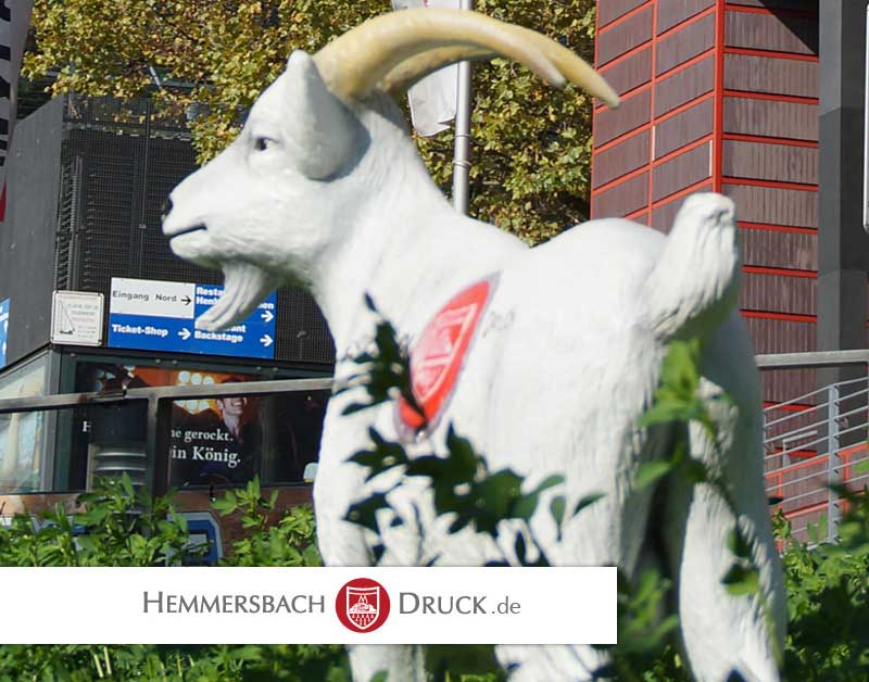 Weiße Ziegenstatue Mit Gelben Hörnern Steht Draußen Bei Grünen Pflanzen Und Stadtschildern.