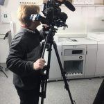 Person Bedient Videokamera Auf Stativ In Raum Mit Weißen Wänden Und Technischem Equipment.