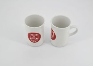 Zwei Sublimationsgeeignete Weiße Keramiktassen Mit Rotem Logo Stehen Auf Weißem Hintergrund, Eine Frontal, Eine Seitlich.