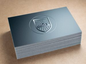 Stapel Edler Schwarzer Visitenkarten Mit Glänzend Geprägtem Wappen-Logo Auf Mattem Karton, Liegend Auf Holzoberfläche