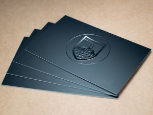 Vier Elegante Schwarze Karten Mit Glänzend Geprägtem Wappen-Logo Auf Mattem Hintergrund, Fächerförmig Angeordnet Auf Holzoberfläche