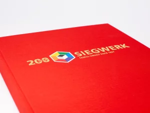 Rotes Hardcover-Buch Mit Goldener Prägung „200 Years Siegwerk – Family-Owned Since 1824“ Und Farbigem Logo – Druckerei Hemmersbach