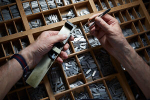 Person Ordnet Metallsatzbuchstaben Mit Pinzette Auf Einem Tisch In Einer Druckwerkstatt An.
