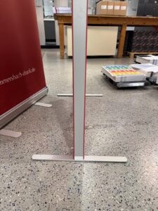 Schmaler, Weiß-Roter Displayständer Mit T-Fuß Aus Metall Auf Gesprenkeltem Boden Zwischen Büroausstattung.