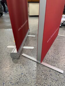 Zwei Rote Werbebanner Mit Metallfüßen Stehen Parallel Auf Einem Grauen, Gesprenkelten Boden.